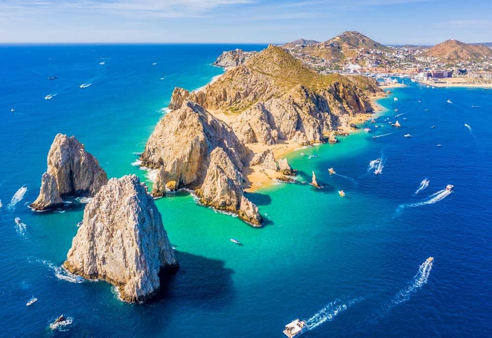 drone shot of lands end in Cabo. It's a sunny day and the sea looks a brilliant view. Lots of small boats can be seen
