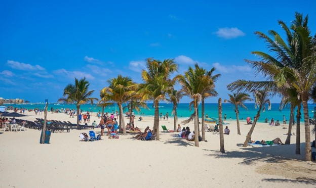 Tropical beach at Playa de Carmen with palm trees, white sand and sunbathers.