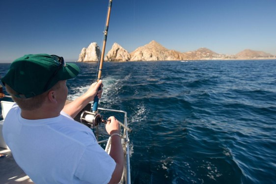 man sports fishing with lands end at cabo visible in background.